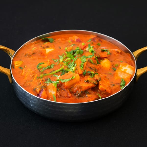 Indian curry with paneer and vegetables in a metal serving bowl with brass handles.
