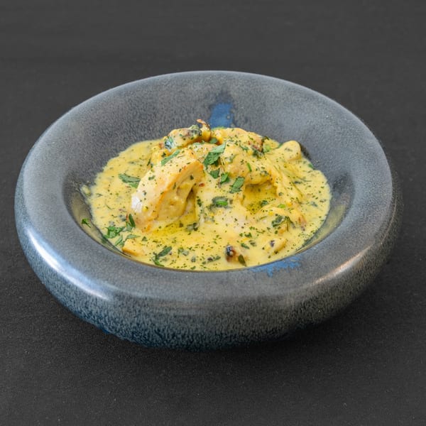 Chicken in a creamy yellow sauce with green herbs, served in a dark blue bowl.