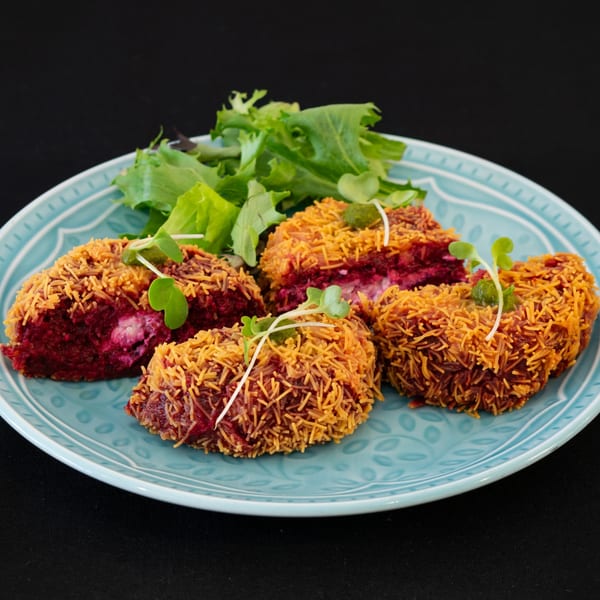 Four beetroot cutlets with crispy vermicelli coating, garnished with microgreens and a side of lettuce.