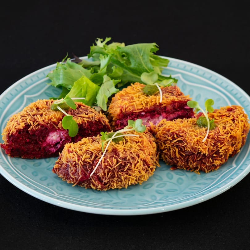 Four beetroot cutlets with crispy vermicelli coating, garnished with microgreens and a side of lettuce.