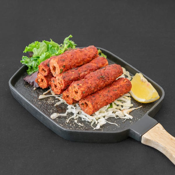 Red seekh kebabs on a black platter with shredded cabbage, lettuce, and a lemon wedge.