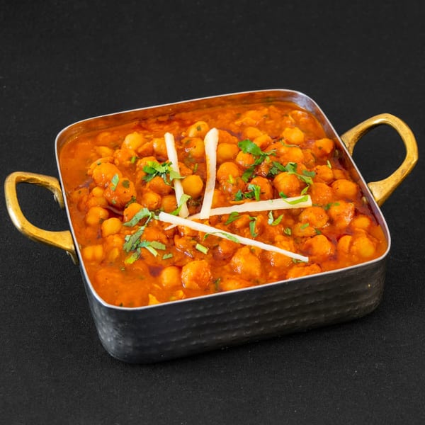 A metal serving dish filled with chana masala, garnished with cilantro and white strips.