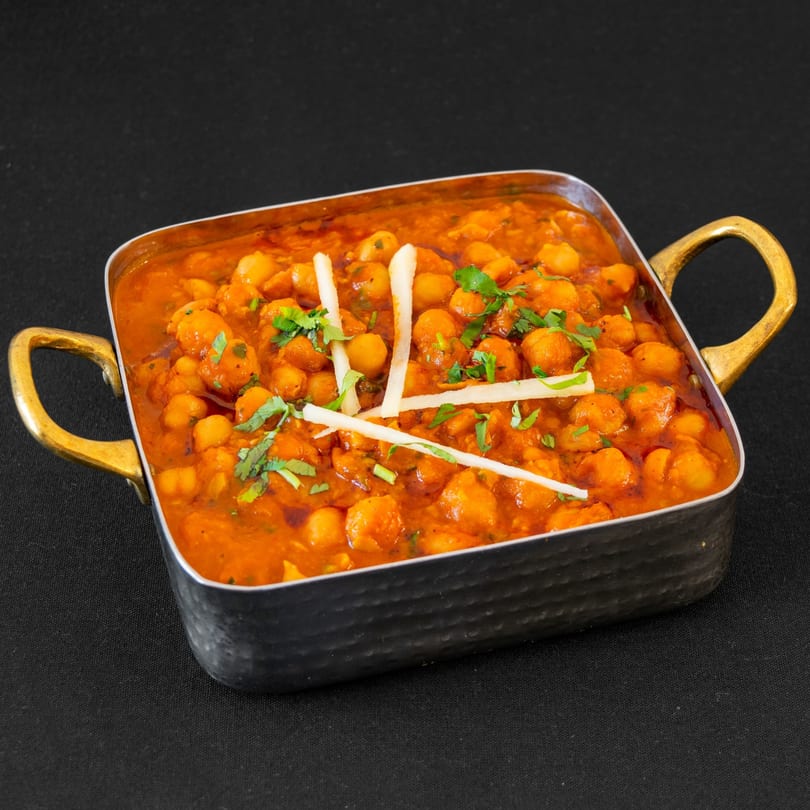 A metal serving dish filled with chana masala, garnished with cilantro and white strips.
