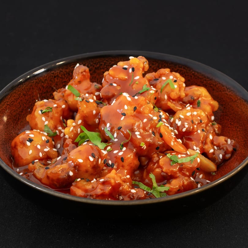 Sweet and sour cauliflower bites, garnished with sesame seeds and fresh herbs, in a rustic bowl.